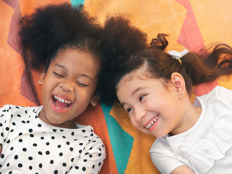 Two young children lying on their backs laughing joyfully with a colorful background.